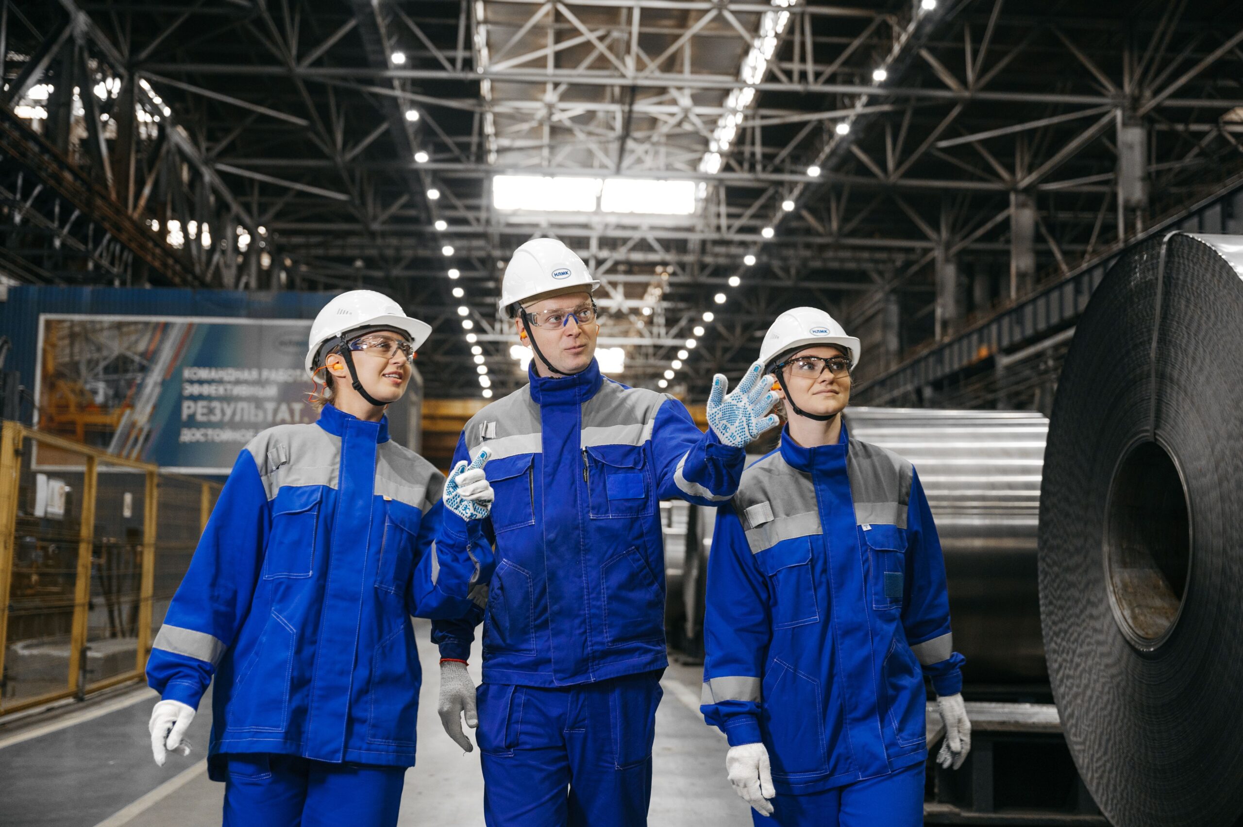 Group of workers in safety gear inside an industrial steel factory, engaging in discussion