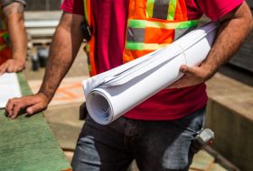 Construction workers in safety vests holding a blueprint