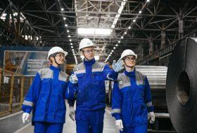 Group of workers in safety gear inside an industrial steel factory, engaging in discussion