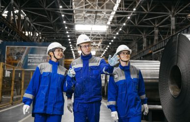 Group of workers in safety gear inside an industrial steel factory, engaging in discussion