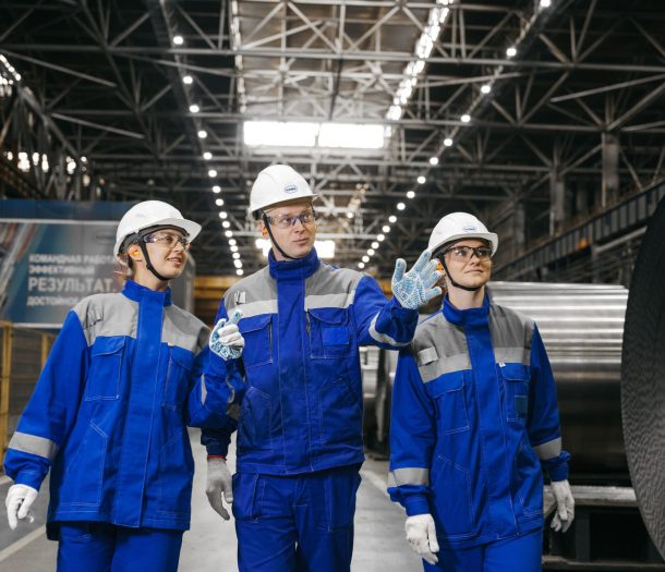 Group of workers in safety gear inside an industrial steel factory, engaging in discussion